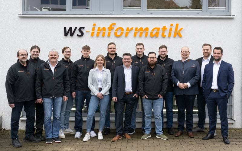 Zu sehen ist ein Gruppenbild von WS-Informatik, versammelt vor dem Firmenschriftzug an der Wand des Geschäftsgebäude.